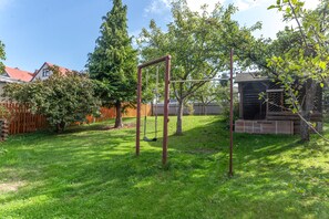 A backyard with a swing set, a wooden playhouse, and a fenced area.