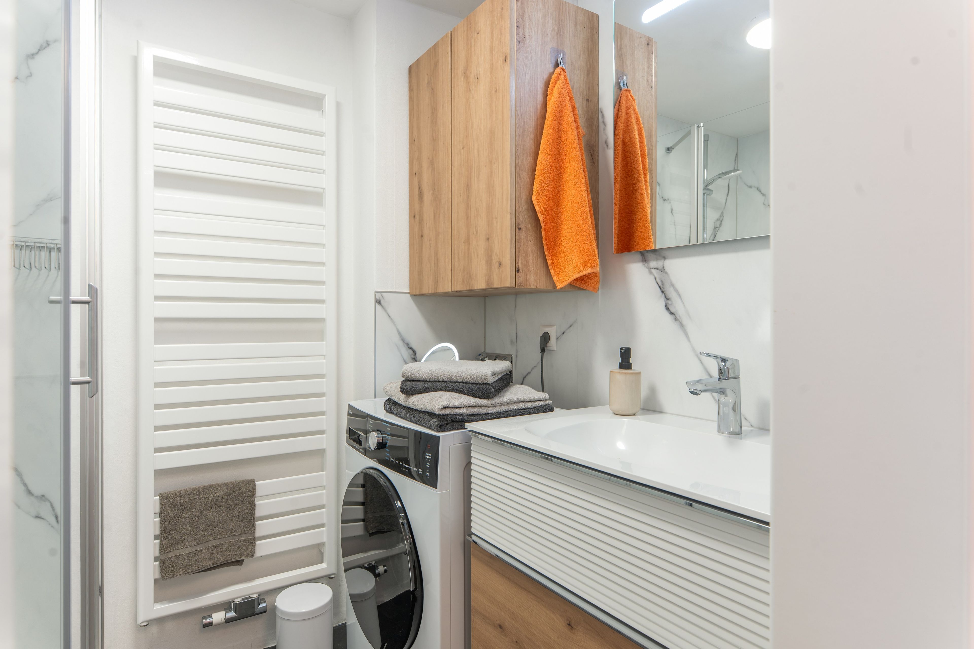 Un baño moderno con lavadora y secadora integradas, un armario de madera, un espejo y un lavabo con grifo.