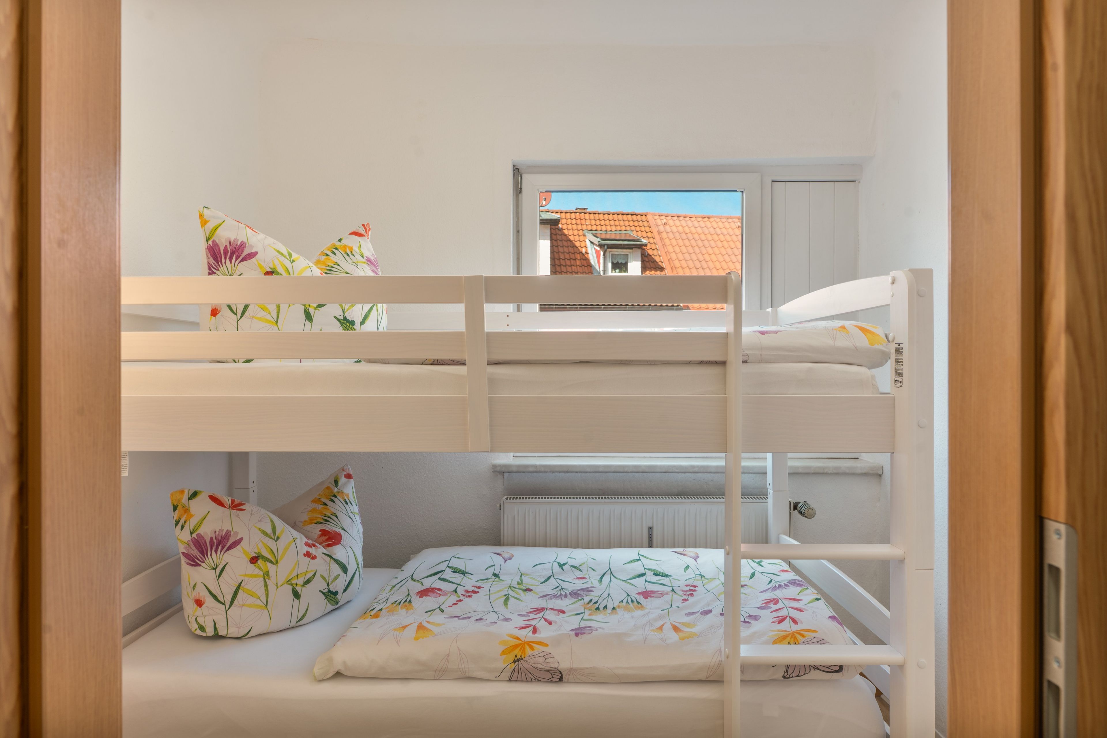 Un letto a castello con biancheria da letto floreale e una finestra che si affaccia su un edificio con tetti rossi.