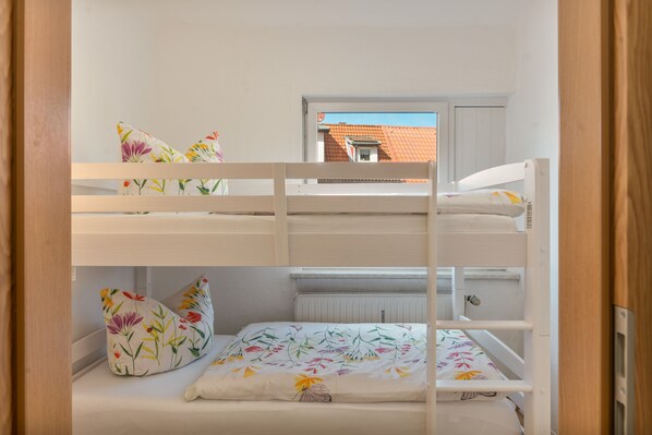 A bunk bed with floral bedding and a window with a view of a red-roofed building.