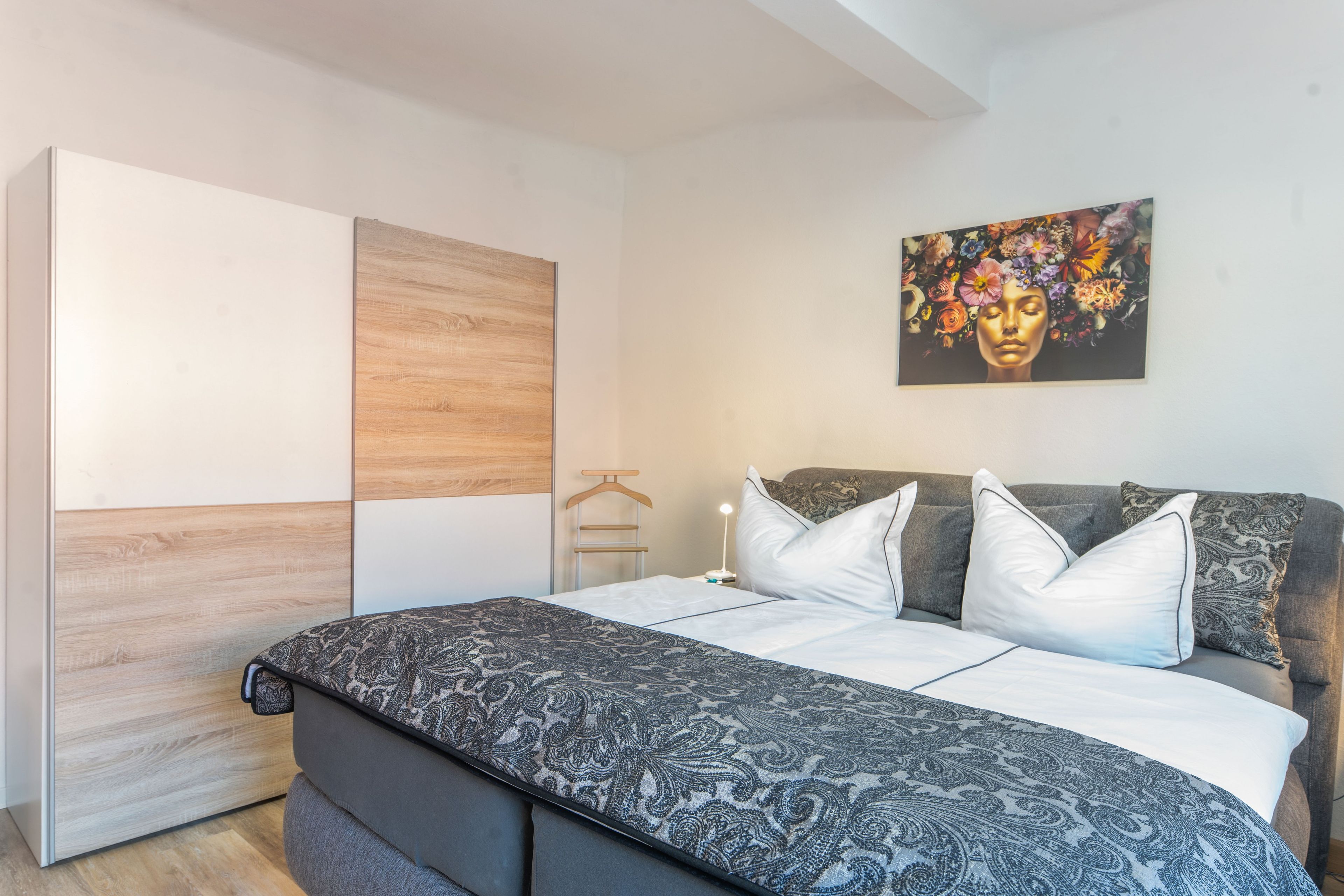 A bedroom with a bed, a wardrobe, a nightstand, and a painting on the wall.