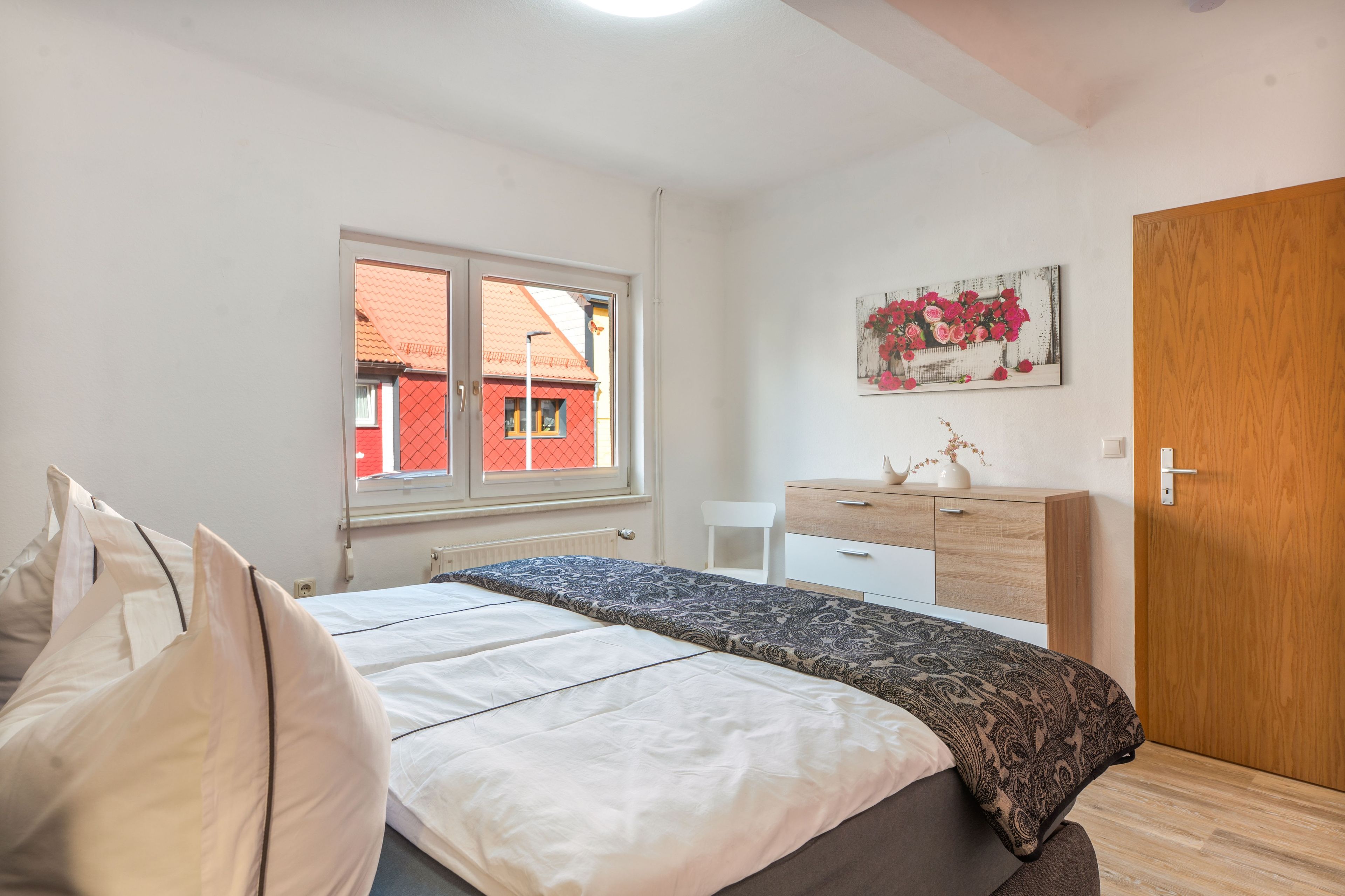 Ein Schlafzimmer mit Bett, Kommode, Fenster und Tür.