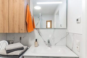 A bathroom with a white sink, a mirror, a wooden cabinet, and a towel rack with an orange towel.