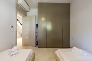 A bedroom with two beds, a wardrobe, and a staircase leading to an upper floor.