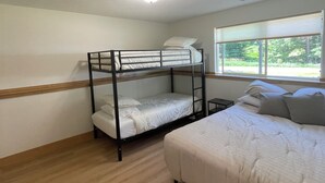 Una habitación con literas, una cama individual, una ventana con persianas y una lámpara en el techo.
