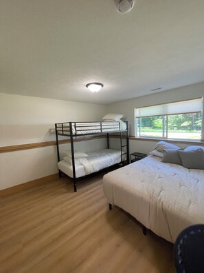 A room with a bunk bed, a single bed, a window with blinds, and a ceiling light. - Welcome to Harrietta Pines – Your Cozy Up-North Family Getaway! (Harrietta)