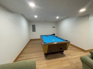 A pool table in a room with wooden flooring and white walls. - Welcome to Harrietta Pines – Your Cozy Up-North Family Getaway! (Harrietta)