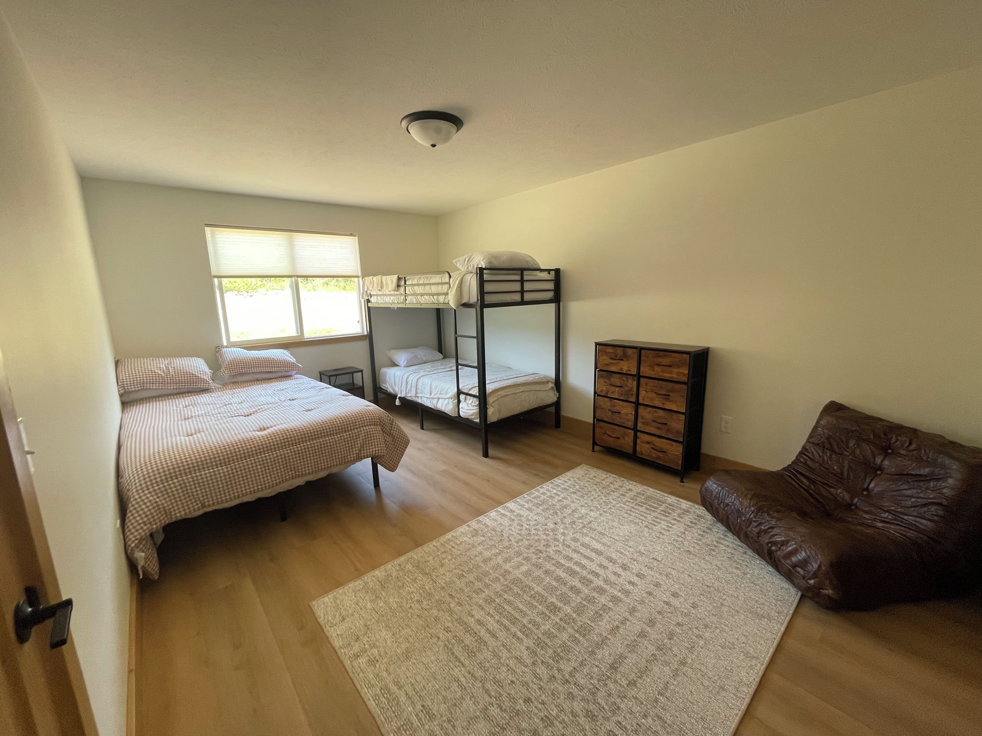 A bedroom with a bunk bed, a chest of drawers, a brown leather sofa, and a large rug.
