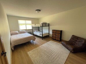 Un dormitorio con una cama litera, un aparador, un sofá de cuero marrón y una alfombra grande.