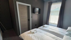 Ett hotellrum med två sängar, en tv som är monterad på väggen, en dörr och ett fönster med gardiner.
