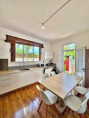 A modern kitchen with a wooden dining table, white chairs, and a view of greenery outside. - Villa B L'oasis tropicale (Riviere du Rempart)