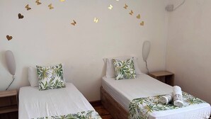 Habitació amb dos llits de fusta, roba de llit blanca, aire condicionat fixat a la paret i ventilador de sostre.
