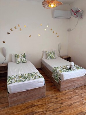 Ein Zimmer mit zwei Holzbetten, weißer Bettwäsche, einer Wand-Klimaanlage und einem Deckenventilator.