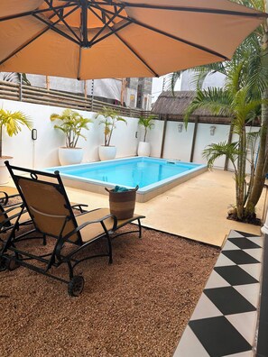 A pool area with a chair and umbrella, surrounded by potted plants and a checkered floor. - Villa B L'oasis tropicale (Riviere du Rempart)