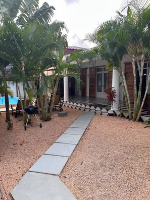 Ein Innenhof mit Schachbrettboden, Palmen, einem Grill und einem Pool.