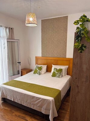 A hotel room with a bed, a bedside table, a hanging lamp, a wall tapestry, and a potted plant. - Villa B L'oasis tropicale (Riviere du Rempart)