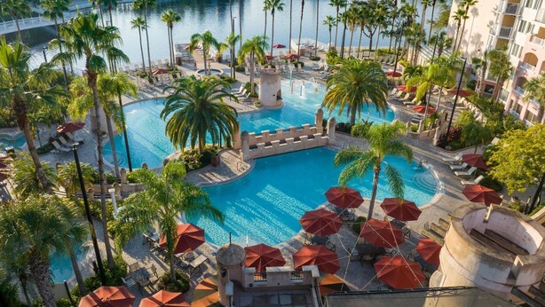 Uma área de piscina em resort, com palmeiras, espreguiçadeiras e guarda-sóis.