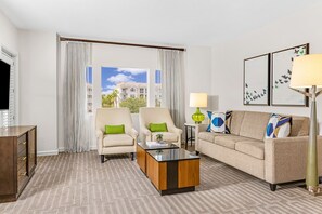 Ein Hotelzimmer mit großem Fenster, zwei Sesseln, einer Couch, einem Couchtisch, einer Lampe und Kunstwerken an der Wand.
