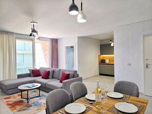 A modern living room with a sofa, dining table, and kitchen in the background. - Beachside Apartment 307 (Gjiri Lalzit)