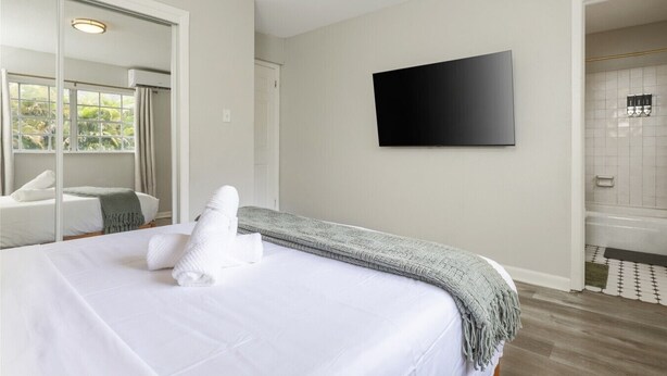 A hotel room with a bed, a television, a bathroom with a shower, and a large mirror. - Cozy 1BR Hideaway w/ FREE Parking · Prime Location (Tampa)
