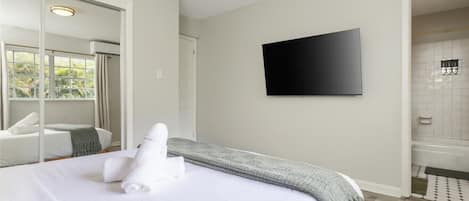 Habitación de hotel con cama, televisión, baño con ducha y un espejo grande.