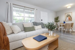 Una sala de estar con sofá, mesa de centro, mesa de comedor, sillas y una planta en maceta.