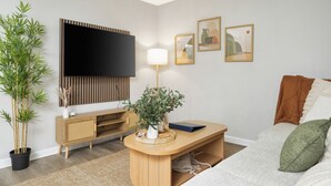 A modern living room with a flat-screen TV, wooden furniture, a potted plant, and framed artwork on the wall. - Cozy 1BR Hideaway w/ FREE Parking · Prime Location (Tampa)