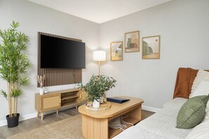 Ein modernes Wohnzimmer mit Flachbildfernseher, Holzmöbeln, einer Topfpflanze und gerahmten Bildern an der Wand.
