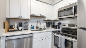 A modern kitchen with white cabinetry, stainless steel appliances, and a built-in dishwasher. - Cozy 1BR Hideaway w/ FREE Parking · Prime Location (Tampa)