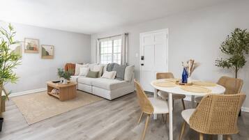 Een woonkamer met een bank, salontafel, eettafel met stoelen en een deur.