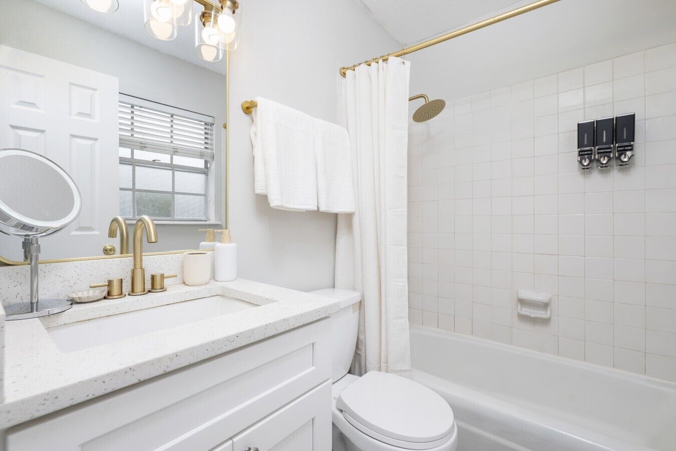 A modern bathroom with a white sink, gold fixtures, a toilet, and a shower area.