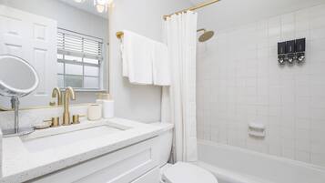 A modern bathroom with a white sink, gold fixtures, a toilet, and a shower area.