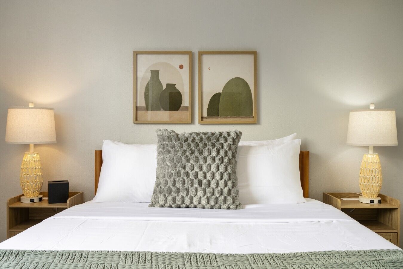 Een hotelkamer met een groot bed, twee nachtkastjes, twee lampen en twee ingelijste foto's aan de muur.