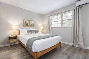 Ein Schlafzimmer mit einem hölzernen Bett, zwei Nachttischen mit Lampen, einem Fenster mit Vorhängen und gerahmten Bildern an der Wand.