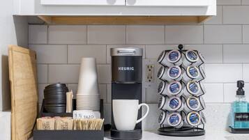 A coffee station with a Keurig coffee maker, disposable cups, a coffee mug, a paper cup holder, and a hand soap dispenser.