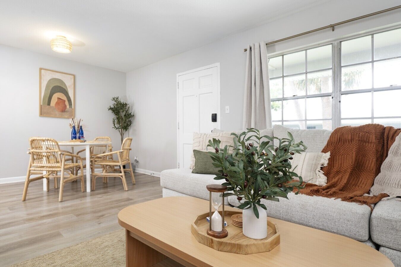 A living room with a sofa, coffee table, dining table with chairs, and a large window with curtains.