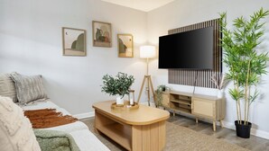 En stue med sofa, sofabord, lampe, fjernsyn og en plante.