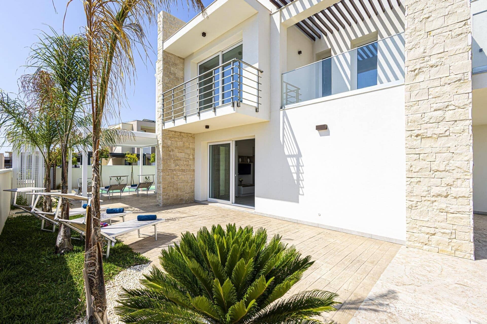 A modern two-story house with a balcony, a patio with outdoor furniture, and a well-maintained garden.