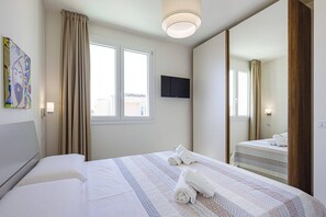 A hotel room with a bed, a television, a large mirror, and a window with curtains. - Villa Selene by Villa Plus (Marzamemi)