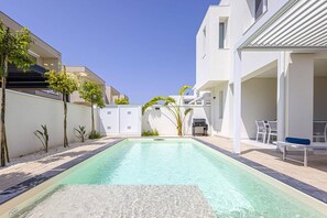 A swimming pool with a tiled deck, surrounded by white buildings, some with balconies. - Villa Selene by Villa Plus (Marzamemi)