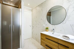 A bathroom with a marble wall, a round mirror, a wooden vanity, and a modern shower enclosure. - Villa Selene by Villa Plus (Marzamemi)