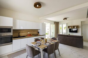 A modern kitchen with white cabinets, a wooden countertop, and a dining area with a table set for four. - Villa Selene by Villa Plus (Marzamemi)