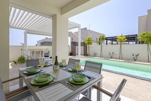 An outdoor dining area with a pool view, white furniture, and decorative bowls. - Villa Selene by Villa Plus (Marzamemi)
