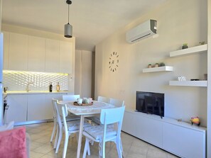 A modern kitchen with white cabinets, a dining table with chairs, a hanging light fixture, and a mounted air conditioner. - Lura 2 Holiday Homes 181 (Gjiri Lalzit)