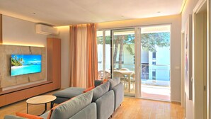 Una sala de estar moderna con un sofá, un televisor montado en la pared y un ventanal corredizo que da a un espacio exterior.