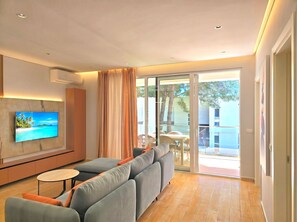 A modern living room with a sofa, a TV mounted on the wall, and a sliding glass door leading to an outdoor area. - White Shell Apartments (Gjiri Lalzit)