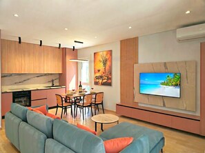 A modern living room with a sofa, dining table, and a TV mounted on the wall. - White Shell Apartments (Gjiri Lalzit)