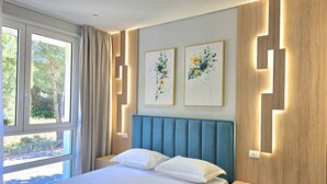 Una habitación de hotel moderna con una cama grande, dos obras de arte colgadas en la pared, una ventana con cortinas y una mesita de noche.