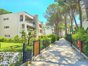 A pathway lined with trees and a building with balconies and a stone facade. - Relax Apartment By The Sea (Gjiri Lalzit)