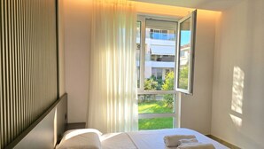 Een hotelkamer met een bed, een raam met gordijnen en uitzicht op groen.